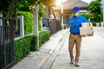 Asian delivery man in blue t-shirt carrying parcel box and document to sign in front of customer home. Delivery man concept.