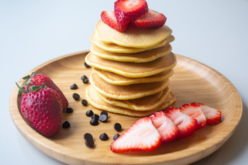 Fluffy breakfast pancakes with chocolate syrup, chocolate chips and fresh ripe strawberries served on a wooden plate