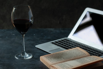Copa de vino tinto, laptop y libro. 