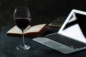 Copa de vino tinto, laptop y libro. 