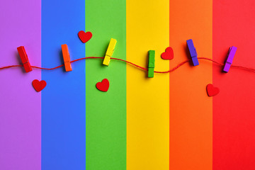 rainbow colored wooden clothespins and red hearts on lgbt flag background. Pride day concept, flat lay