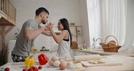 Cute interracial couple wearing pajama is dancing and singing while preparing dough for their lunch, spending time together - recreational pursuit concept 4k