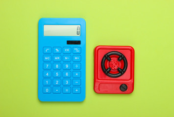 Calculation of gas or electricity costs. Calculator and toy kitchen stove on green background. Top...