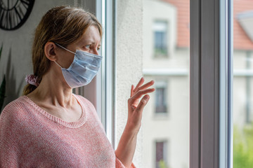 Femme regardant par la fenêtre. Portant un masque chirurgical