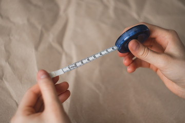 Woman holds centimeter measuring tape in hands on craft paper background.