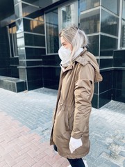 Stylish young women in a flu mask and protective gloves against coronavirus walks on the street and looks away. Covid-19.