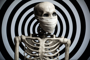A skeleton wearing a cloth medical face mask in front of a hypnotic spiral background. Conspiracy or confusion over the covid-19 coronavirus pandemic.