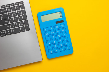 Calculator and laptop on a yellow background. Top view