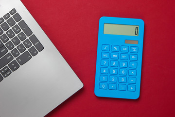 Calculator and laptop on red background. Top view