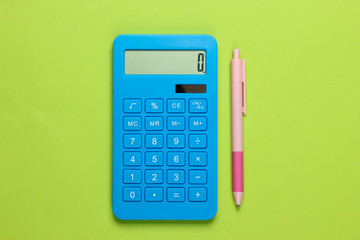 Blue calculator with pen on green background. Top view.