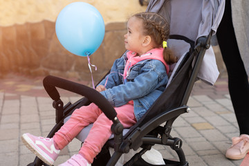 A little Caucasian girl sits in a pram and holds an inflatable ball in her hand.
