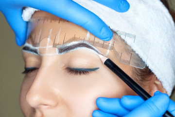 Permanent make-up for eyebrows of beautiful woman with thick brows in beauty salon. Closeup...