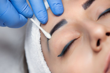 Permanent make-up for eyebrows of beautiful woman with thick brows in beauty salon. Closeup beautician doing  tattooing eyebrow. Makeup and Cosmetology concept.