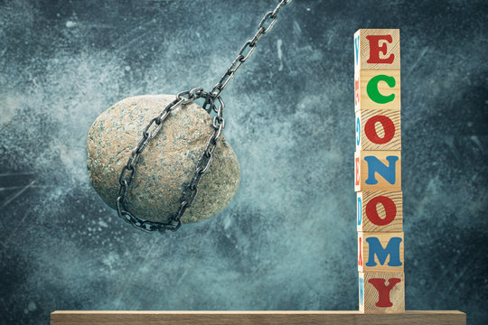 Blow to world economy concept. Stone hanging on a chain sways towards economy spelled in letters on wooden blocks.