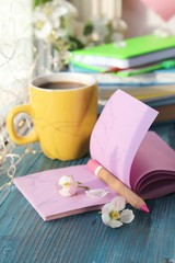 Fototapeta na wymiar Cup of coffee, blank notebook for notes, a stack of books, apple flowers on a wooden windowsill, home comfort concept