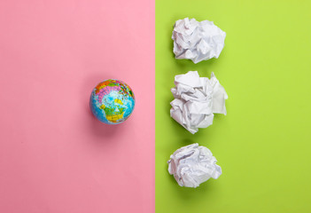 Globe with crumpled paper balls on green pink background. Top view. Concept art.