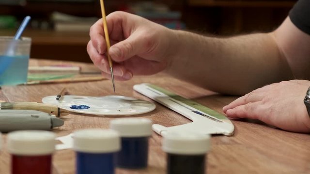 master applies paint onto wooden part of passenger jetliner model with brush at table in room close view slow motion