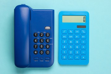Calculator with a stationary office phone on a blue background. Top view