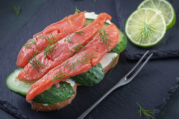 Salted salmon sandwich with cream cheese and cucumber on slate platter closeup