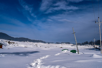 A landscape of clear blue skies & snowfield with small green wooden bridge & extention poles buried under the heavy snow. World famous ski destination Gulmarg in extreme winter in Kashmir, India.