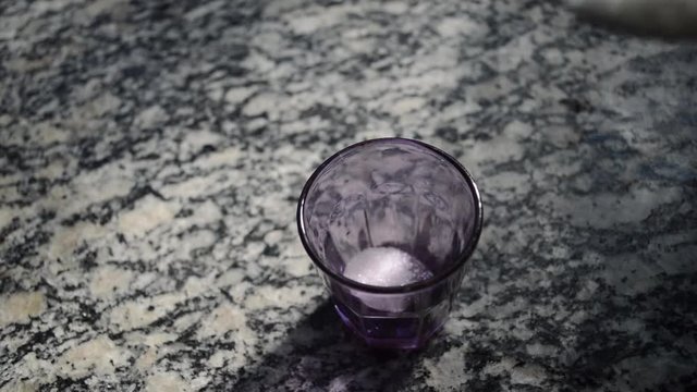 woman filling small purple colored cup with several spoons of white sugar
