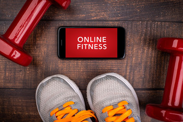 Gray sneakers, red dumbbell and smartphone on a woodan background. App for training indoors. Online Fitness program. Home online workout. Top view, Covid-19 Coronavirus quarantine concept