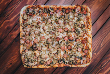Homemade pizza with sausages, mushrooms, cheese and onions lies on a mahogany table. The concept of lunch, fast food and Italian cuisine.