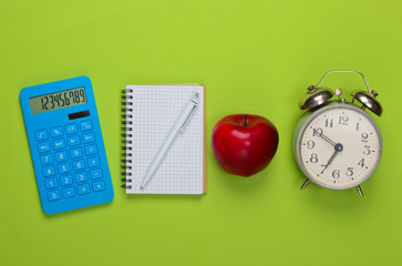 Calculator with notebook, apple, alarm clock on green background. Back to school. Education concept. Top view
