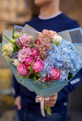 Strong man holding a delicate bouquet of beautiful flowers in his hands. Delicate flower bouquet. Wrapped flowers bouquet. Fresh beautiful flower. Man holding a big beautiful flowers bouquet.