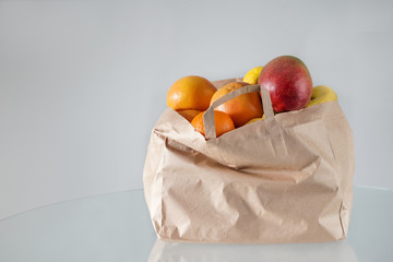 Fruit delivery. Citruses, kiwi, mango in a craft paper bag on the table. Stay at home. Coronavirus, quarantine, isolation