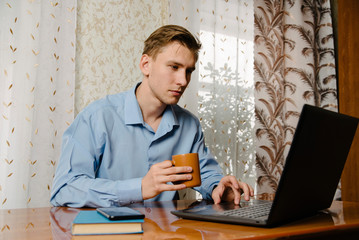 Man working online from home on his laptop, drinking coffee at home at a Desk