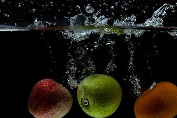 Fototapeta na wymiar View of colorful fruits falling in water on black background. Gorgeous backgrounds.