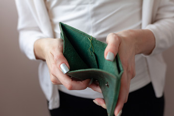 A girl in a protective mask holds a purse. Green purse in women's hands. The concept of poverty and bankruptcy