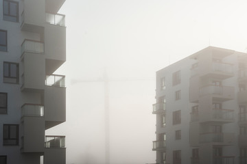 Construction cranes between apartment buildings in a foggy morning