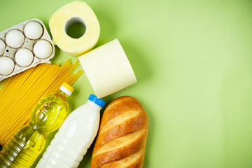 Essential fresh products lie on a green background. Eggs, greens, spaghetti, sunflower oil, bread, milk, toilet paper, cookies. Food delivery covid-19 epidemic, Donation. top view. Copy space.