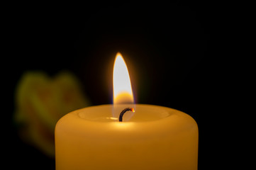 Close up of burning yellow wax candle and rose