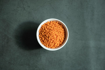 Red lentil in white porcelain bowl on stone, concrete background. Healthy, organic and delicious raw cereal. Top view, flat lay.
