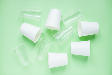 The layout on a green background from white paper and plastic disposable cups. Caring for the environment. Recycling and sorting of garbage. Disposable tableware. Environmental pollution.