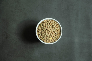 Obraz na płótnie Canvas Green raw lentil in white porcelain, ceramic bowl on concrete, stone background. Healthy and organic cereal. Top view, flat lay.