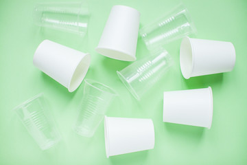 The layout on a green background from white paper and plastic disposable cups. Caring for the environment. Recycling and sorting of garbage. Disposable tableware. Environmental pollution.
