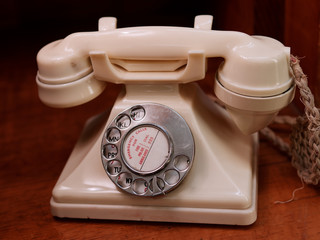Close-up of antique white rotary telephone on a woodern desk.