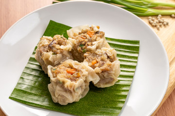 Close up Asian Steam  Dumplings  or Dim Sum a Famous Chinese Food  with Pork and Shrimp on Banana Leaf and  Cutting Wood Board with Garlic, Spring Onion and Peppers.