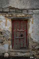 Stone wall with a large red ruined window with blinds and old cables hanging around.