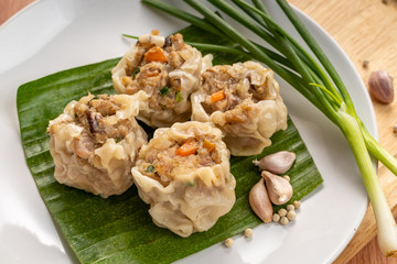Close up Asian Steam  Dumplings  or Dim Sum a Famous Chinese Food  with Pork and Shrimp on Banana Leaf and  Cutting Wood Board with Garlic, Spring Onion and Peppers.