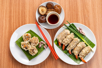 Close up Asian Steam  Dumplings  or Dim Sum a Famous Chinese Food  with Pork and Shrimp on Banana Leaf and White Dish on Wood Table with Spciy Ingredient.