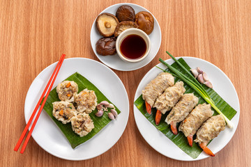 Close up Asian Steam  Dumplings  or Dim Sum a Famous Chinese Food  with Pork and Shrimp on Banana Leaf and White Dish on Wood Table with Spciy Ingredient.