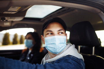 Fototapeta na wymiar Man driving a car wearing sterile medical mask. Taxi driver with a passanger stuck in a traffic jam during coronavirus quarantine isolation in the city. Prevernt spread of covid-19 concept.