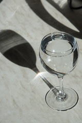 A tall glass stands on the table in the sun. The glass forms a shadow, an interesting geometric pattern. There's water in the glass. Vertical orientation