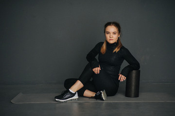 Fototapeta na wymiar Serious caucasian female sportswoman uses a foam roller for relaxation, stretching muscles and back pain in workout in pilates studio. Set photo with film photo gain.