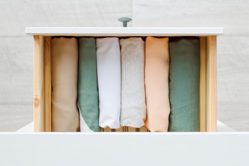 Fototapeta na wymiar women's clothing in natural colors: white, green, beige and orange-pink neatly folded vertically in a drawer, top view